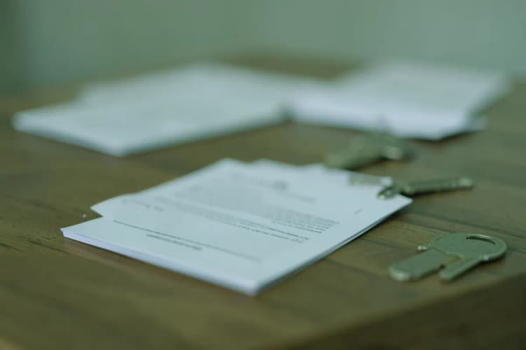 Documentos e chaves sobre uma mesa de madeira com um contrato ao fundo