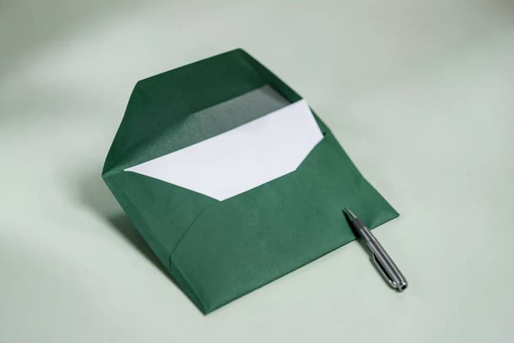Um envelope de carta aberto com uma folha de papel dentro e uma caneta ao lado