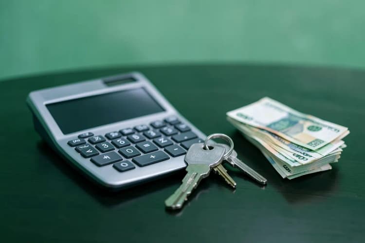 Calculadora ao lado de chaves de um apartamento e notas de dinheiro dobradas sobre uma mesa de madeira