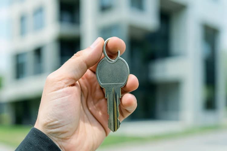Mão segurando uma chave de apartamento com um prédio ao fundo desfocado