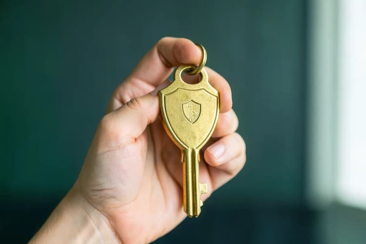 Uma mão segurando uma chave de casa com um escudo dourado em sua volta.