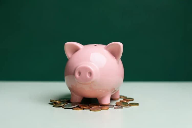Um cofrinho em forma de porquinho com moedas saindo dele.