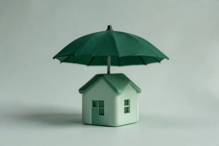 Uma casa em miniatura sendo protegida por um guarda-chuva.